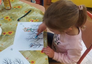 Zdjęcie przedstawia dziewczynkę, która maluje korony drzew
