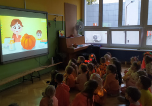 Zdjęcie przedstawia dzieci, które oglądają bajkę edukacyjną o dyni