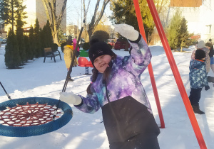 Zdjęcie przedstawia dziewczynkę, która bawi się śniegiem