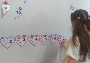 Zdjęcie przedstawia dziewczynkę, która dopasowuje ilość serc do cyfry