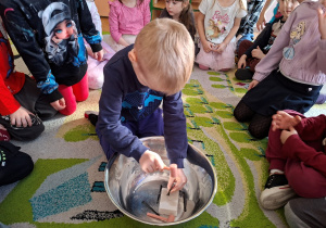 Zdjęcie przedstawia chłopca, który próbuje wydobyć dinozaura