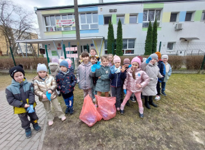 Zdjęcie przedstawia dzieci podczas akcji sprzątania terenu wokół przedszkola