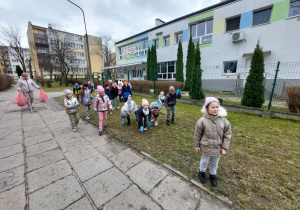 Zdjęcie przedstawia dzieci podczas akcji sprzątania terenu wokół przedszkola