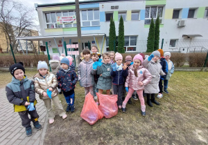 Zdjęcie przedstawia dzieci podczas akcji sprzątania terenu wokół przedszkola